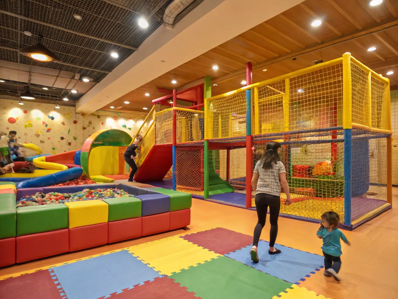 A brightly colored, custom-designed soft play structure with various climbing elements and slides, set in a commercial play area. The image should convey a sense of fun, safety, and innovative design.